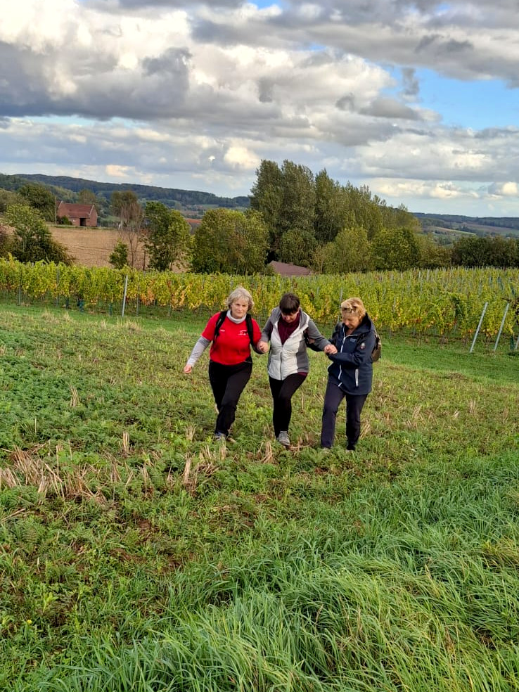 Deux bénévoles soutiennent une randonneuse, elles marchent au bord d'un champ
